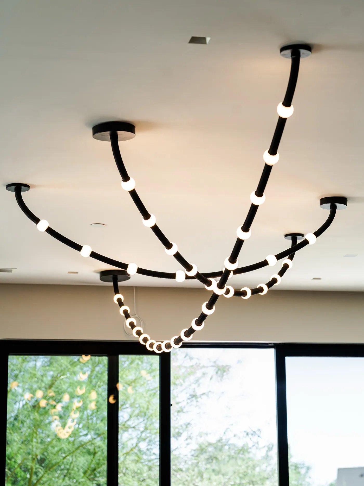 Custom lighting design for modern San Francisco homes | PHX Interior Design Custom lighting design for modern San Francisco homes: custom black-cord ceiling light with glowing spherical globes suspended from multiple canopies in front of tall windows and a palo verde tree