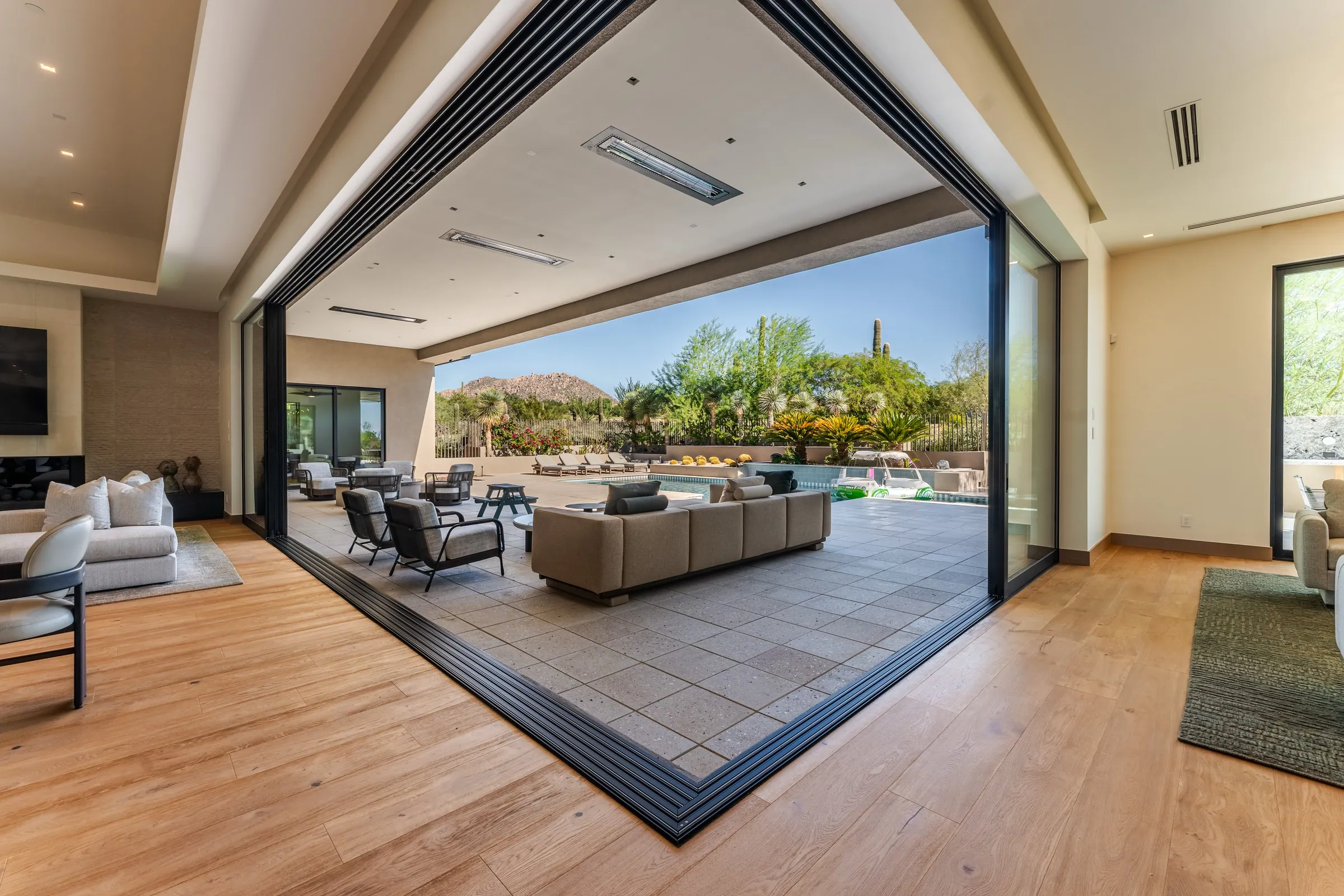 Indoor-outdoor living design for San Francisco luxury residences with pocketing glass walls | PHX Interior Design Indoor-outdoor living design for San Francisco luxury residences with pocketing glass walls: living room with a corner pocketing glass wall fully open to a covered patio, pool and mountains beyond, with oak plank floors and linear heaters overhead
