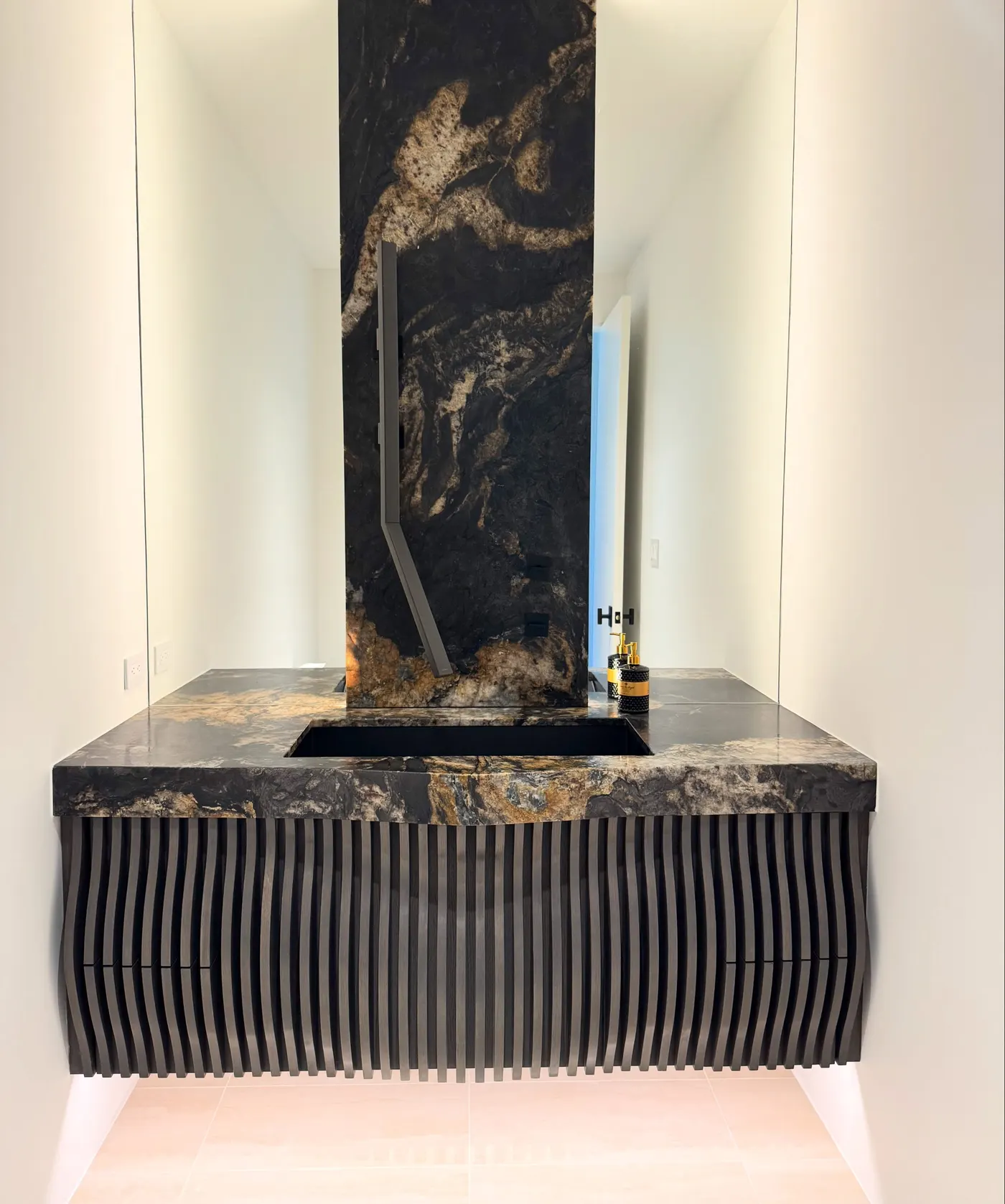 Luxury powder room design in Scottsdale, AZ | PHX Interior Design Luxury powder room design in Scottsdale, AZ: powder room with a dark gold-veined natural stone slab, a wall-mounted faucet and a floating vanity with wavy fluted wood slats