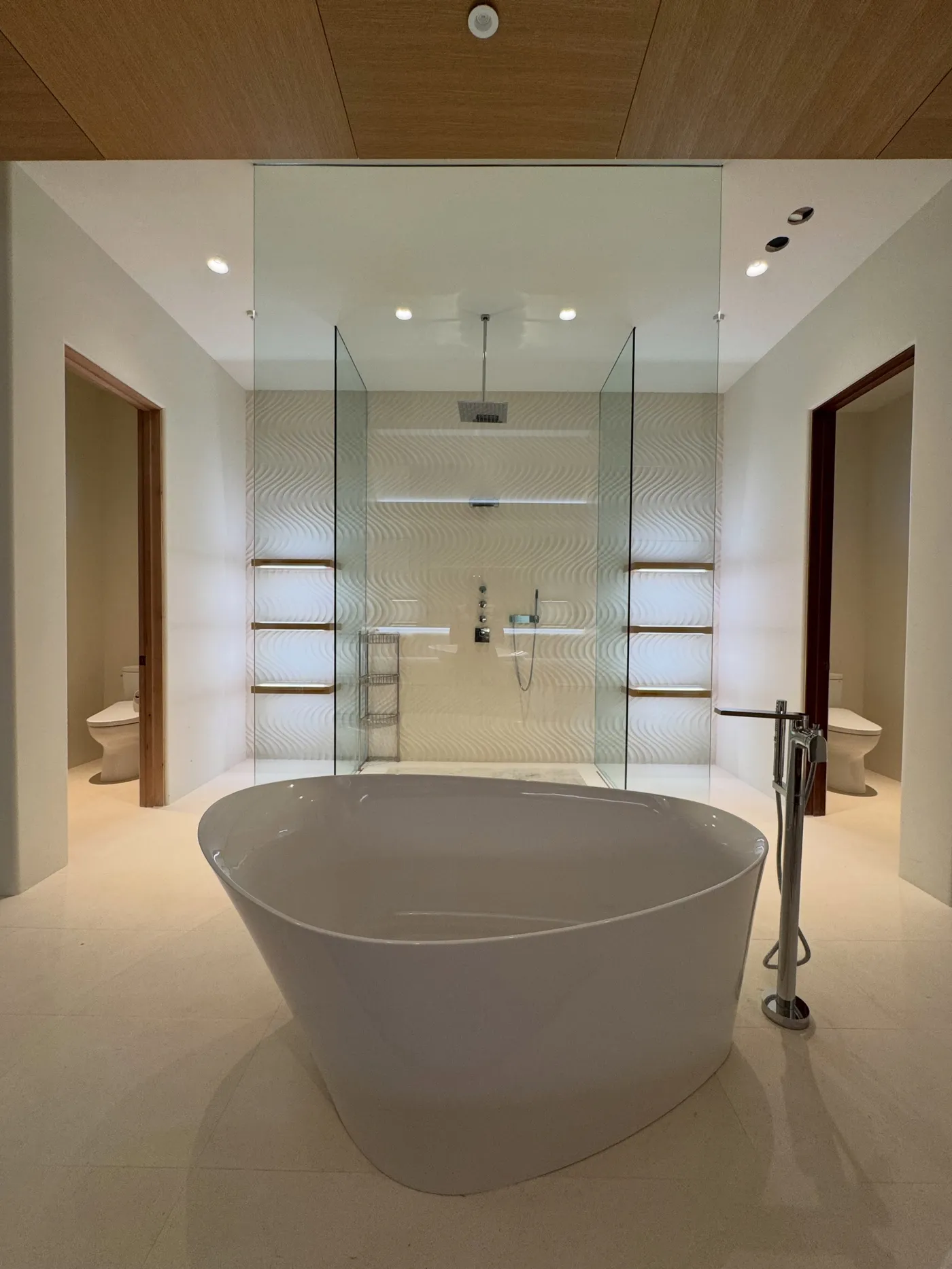 Luxury primary suite bathroom design in Scottsdale | PHX Interior Design Luxury primary suite bathroom design in Scottsdale: primary suite bathroom with a sculptural freestanding tub, a glass-enclosed wet room with wave-sculpted tile and backlit wood shelves, and a white oak ceiling